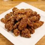 Crispy double-fried chicken wings coated in garlic butter honey glaze, garnished with sesame seeds.