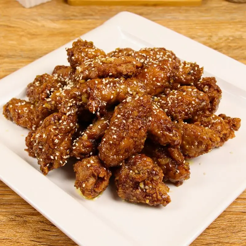 Crispy double-fried chicken wings coated in garlic butter honey glaze, garnished with sesame seeds.