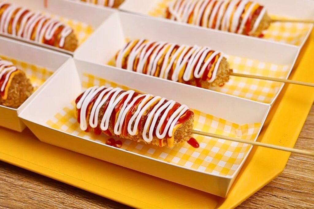 Crispy corndog on a skewer topped with mayo and ketchup
