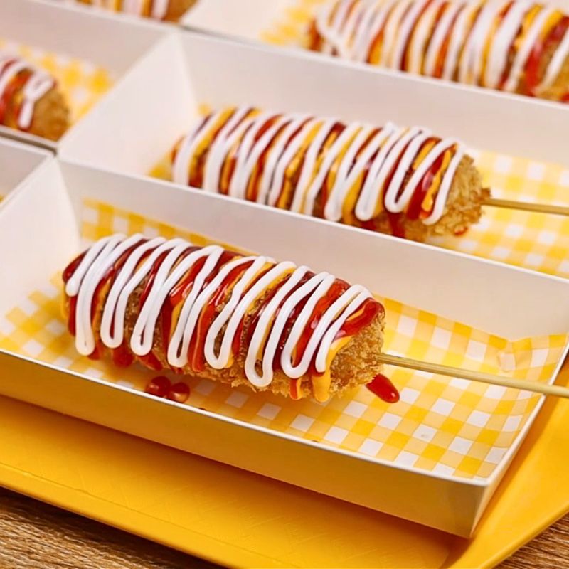 Crispy corndog on a skewer topped with mayo and ketchup