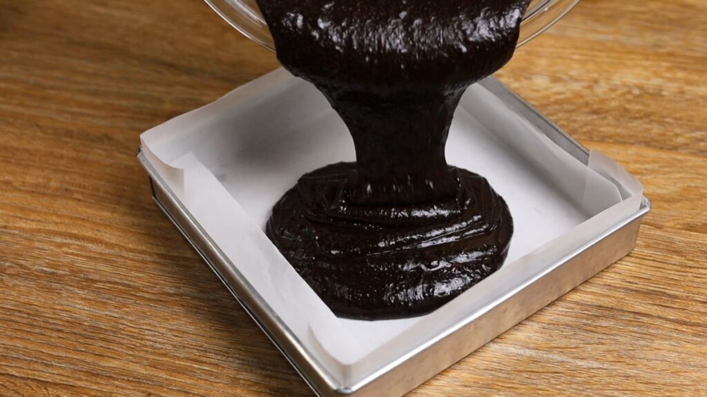 Pouring brownie batter into a parchment-lined baking pan before baking