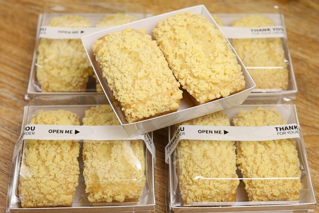 Lemon Crumb Loaf packaged in a 4×4-inch pastry box with a clear cover, showing one freshly baked mini lemon loaf with buttery crumb topping.