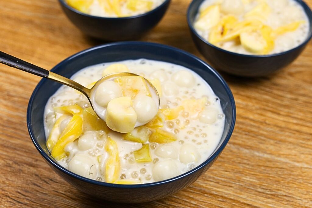 A serving bowl of creamy Ginataang Bilo-Bilo with glutinous rice balls, sweet potatoes, saba bananas, tapioca pearls, and jackfruit scooped with a spoon.