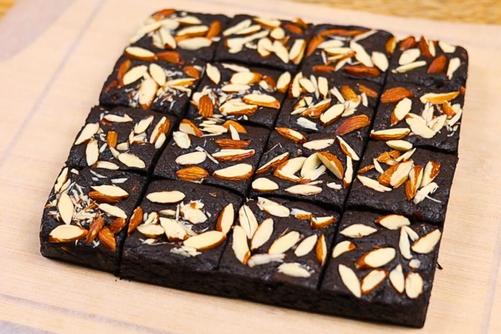 Eggless almond brownies removed from the pan and plated on a wooden chopping board lined with parchment paper.